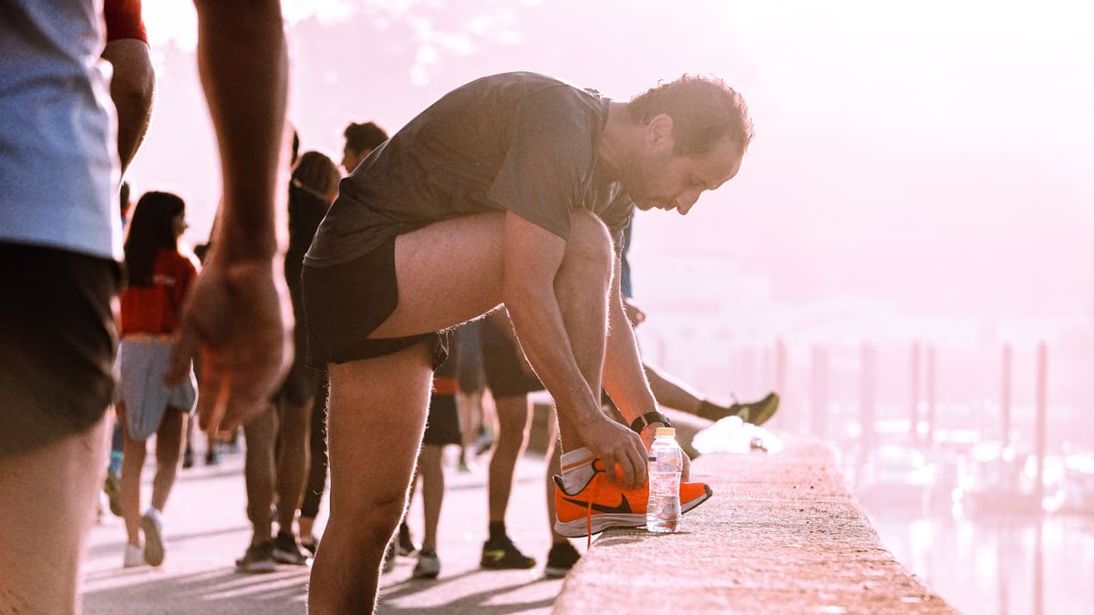 Man ties his shoes before a run outdoors with a bottle of water nearby.